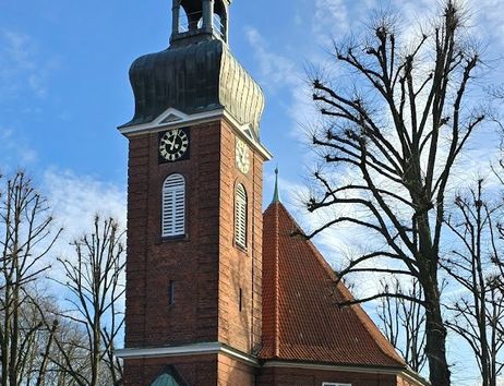 Eine Backsteinkirche mit einem hohen Turm und einer grünen Kuppel unter blauem Himmel.