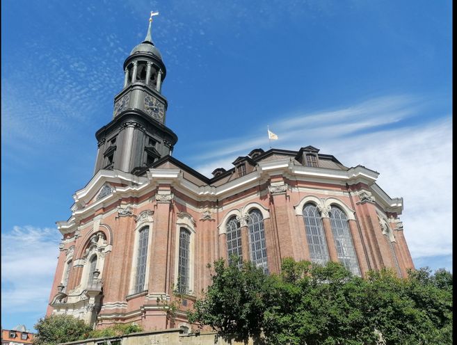 Die St. Michaelis Kirche in Hamburg mit ihrem markanten Turm und der barocken Fassade vor einem blauen Himmel.
