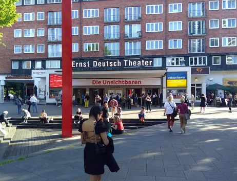 Menschen versammeln sich vor dem Ernst Deutsch Theater in Hamburg bei sonnigem Wetter.