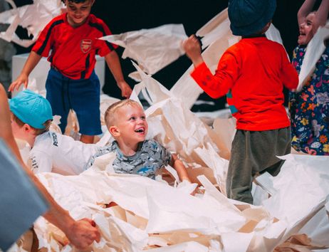 Kinder spielen fröhlich in einem Raum voller zerknülltem weißem Papier und haben sichtlich Spaß dabei.