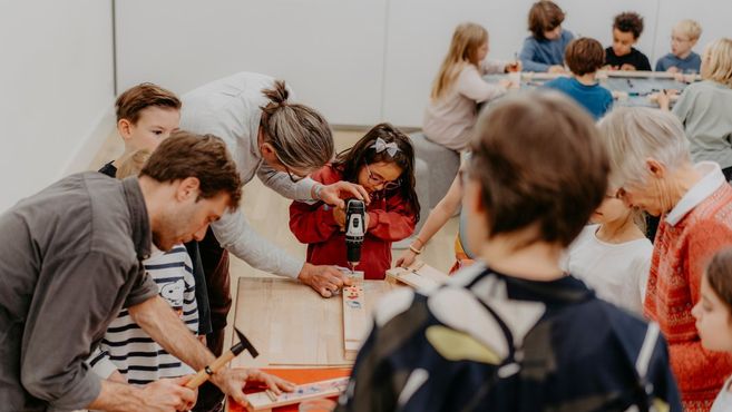 Kinder und Erwachsene arbeiten gemeinsam an einem Holztisch mit Werkzeugen.