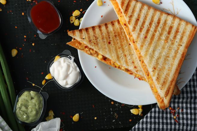 Zwei gegrillte Sandwiches auf einem weißen Teller mit drei verschiedenen Dips daneben.