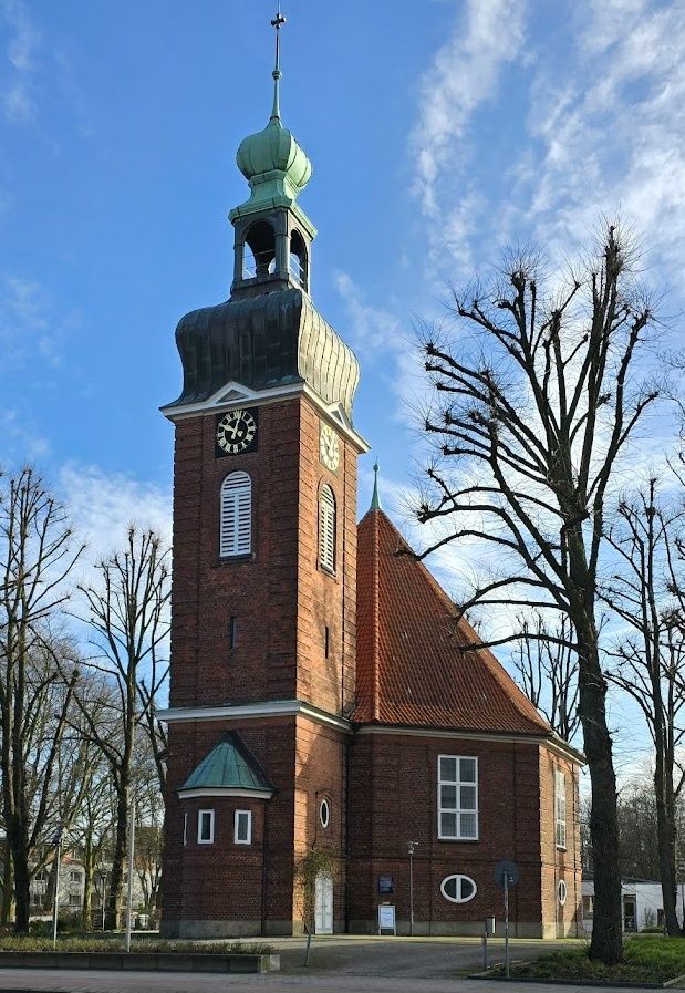 Eine Backsteinkirche mit einem hohen Turm und einer grünen Kuppel unter blauem Himmel.