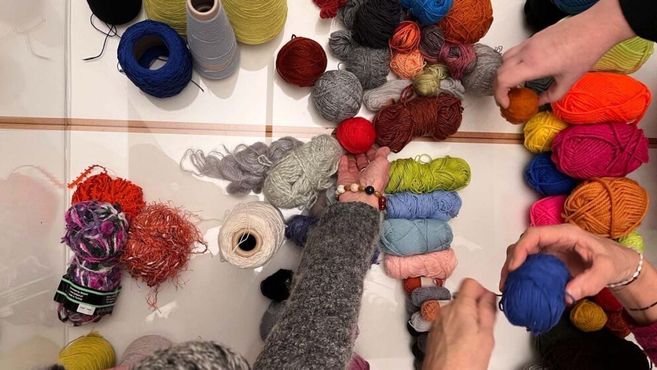 Hände ordnen bunte Wollknäuel auf einem Tisch; passend zum Titel „Die neue Masche - Häkelgespräche im Altonaer Museum“.