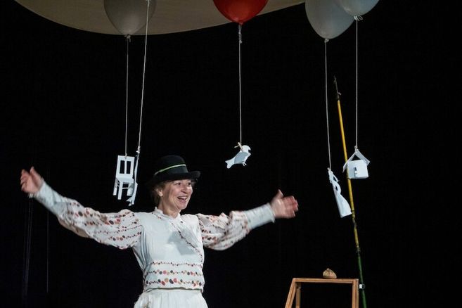 Eine Person in traditioneller Kleidung steht auf einer Bühne mit schwebenden Papierfiguren und Ballons.