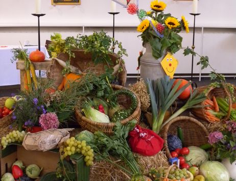 Erntedankfest mit reich geschmücktem Altar, Sonnenblumen, Kerzen, Ikonen und vielen Körben voller Obst, Gemüse und Getreide.