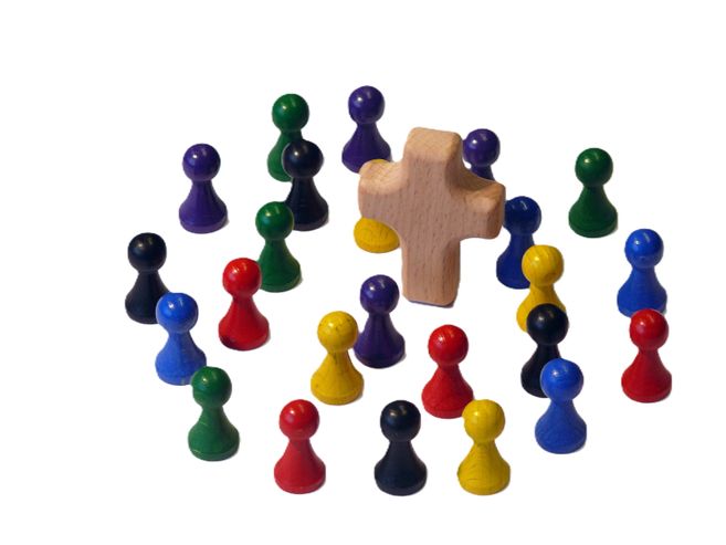 Bunte Spielfiguren um ein hölzernes Kreuz angeordnet.