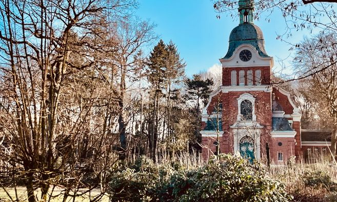 Eine historische Backsteinkirche mit Turm, umgeben von Bäumen im Luthergarten.