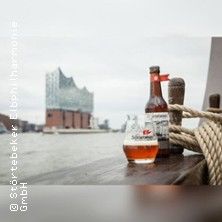 Eine Flasche und ein Glas Störtebeker Bier auf einem Tisch mit der Elbphilharmonie im Hintergrund.