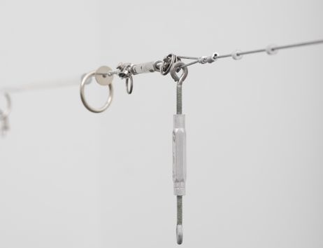 im Vordergrund ist ein quer-gespannter Drahtseil zu sehen, welches durch an ihr befestigte verschiedene Arten von Ringen, Muttern, Haken, sogenannte Hardware, aufgespannt wird. Hintergrund ist verschwommen.