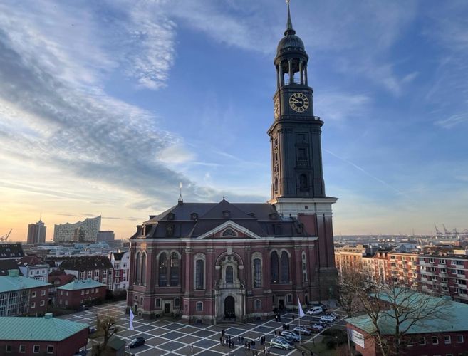 Blick auf die St. Michaelis Kirche in Hamburg bei Sonnenuntergang, mit der Elbphilharmonie im Hintergrund.
