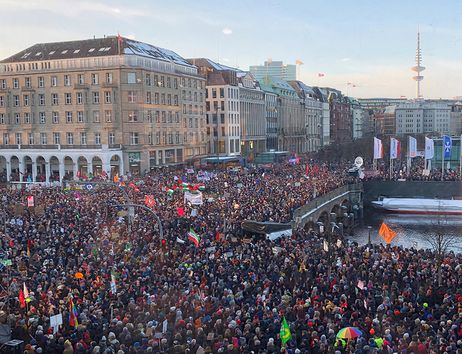 Große Menschenmenge bei einer Demonstration in einer Innenstadt am Wasser, mit vielen Fahnen und Transparenten; im Hintergrund ist der Fernsehturm Hamburg zu sehen.
