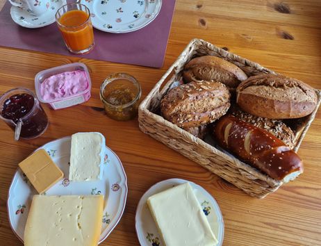 Frühstückstisch mit Brötchen, Käse, Marmelade und Saft.