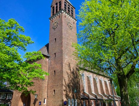 Backsteinkirche mit hohem Turm und grünen Bäumen im Vordergrund.