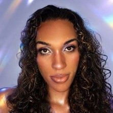 Porträt einer Person mit lockigem Haar und schimmerndem Make-up vor einem holografischen Hintergrund.